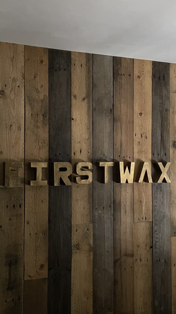De houten wand met de gouden letters First Wax in de studio in Beesd